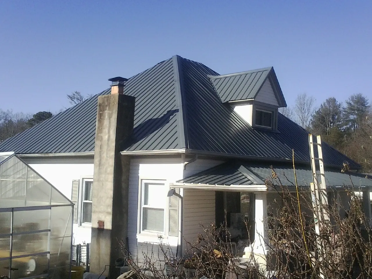 Dark blue standing seam metal roof on a white farmhouse with dormer — Slate & Tile Roof Repair by Roofing Brothers in Sanders