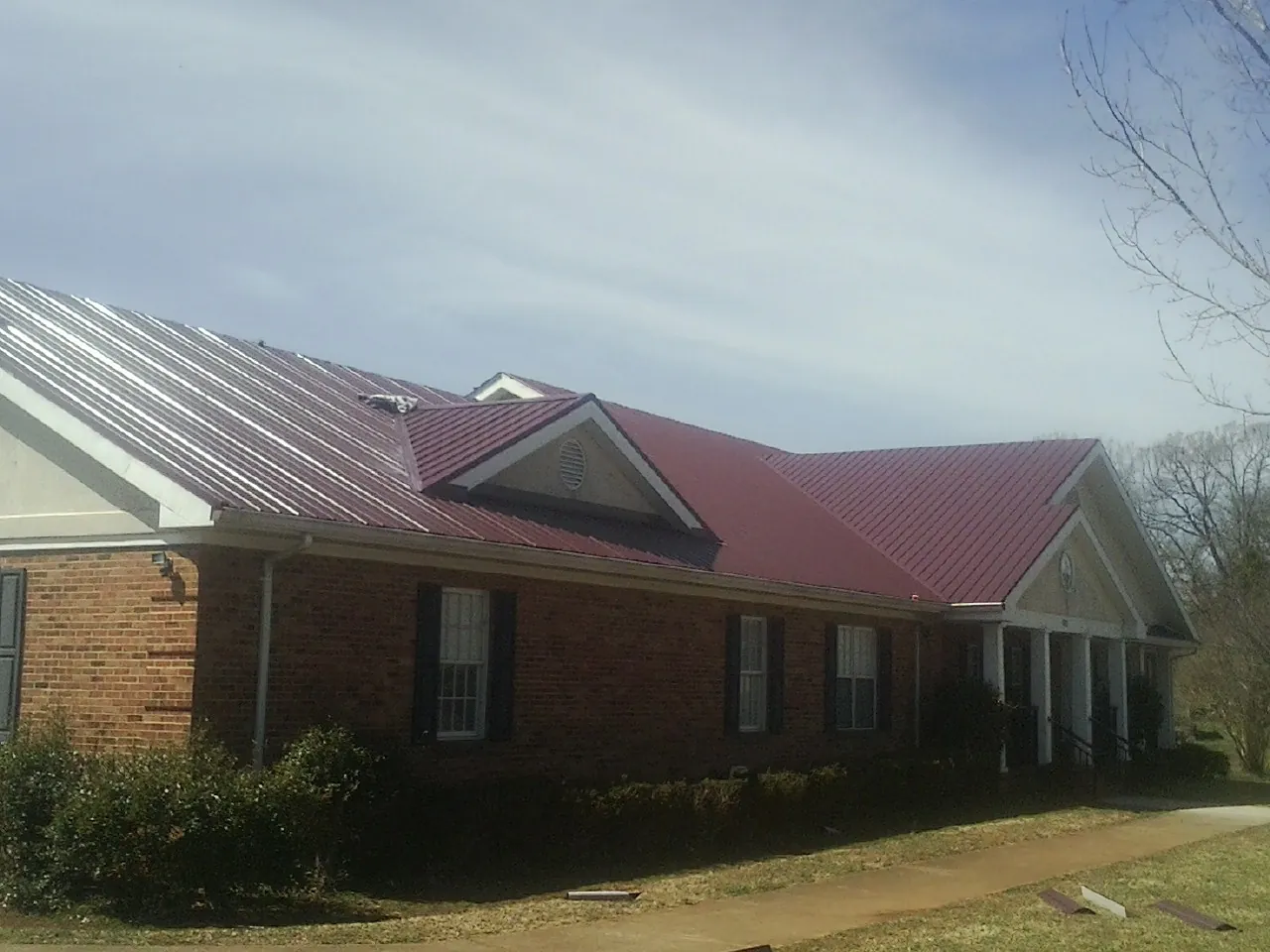 Red metal roof with gabled entries on a long brick building, from a Hail Damage Roof Repair job in Sanders