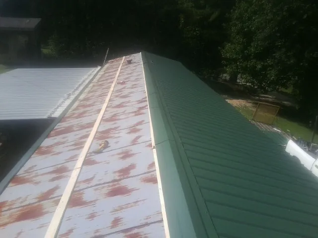 Old rusted panels beside newly installed green metal roofing — Wind Damage Roof Repair by Roofing Brothers in Sanders