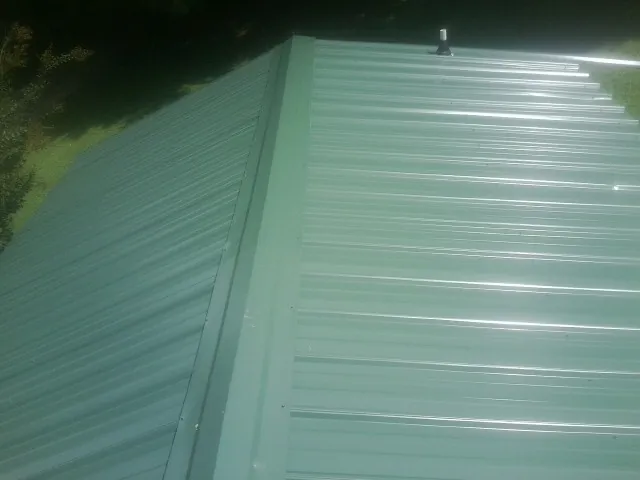 New green metal panels meeting at the ridge of a roof — Flat Roof Repair work by our crew in Sanders
