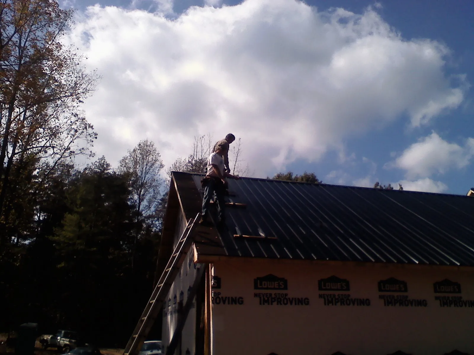 Roofer fastening dark metal panels high against a cloudy sky, from a Roof Inspection job in Sanders