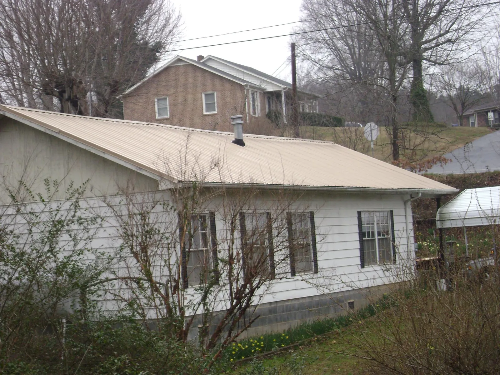 Tan metal roof on a white sided house set into a hillside — Commercial Roofing by Roofing Brothers in Sanders
