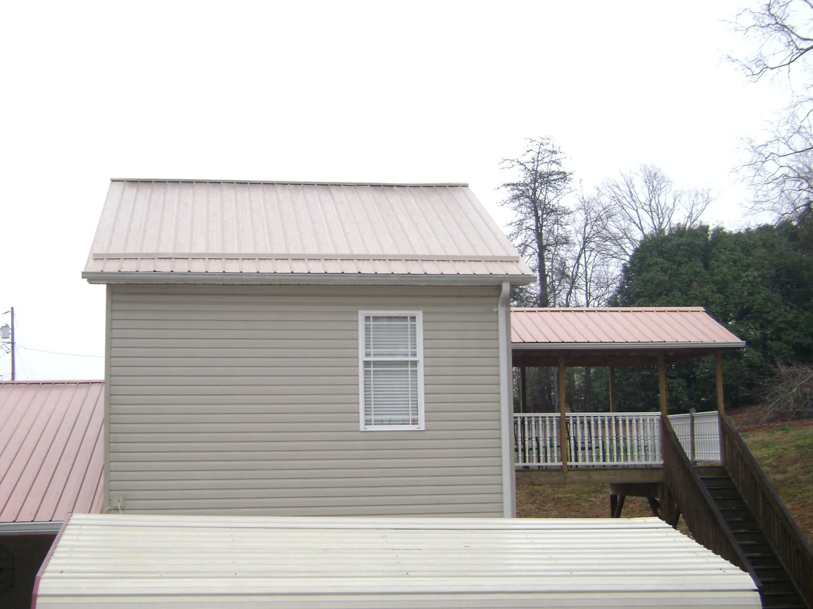 Tan metal roofs on a two story addition and attached porch, from a Roof Replacement job in Sanders